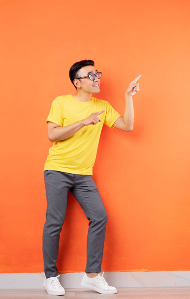 Повна фотографія азіатського чоловіка в жовтій сорочці на помаранчевому тлі. - Фото, зображення