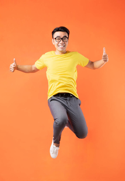 Азійський чоловік у жовтій футболці стрибає на помаранчевому фоні - Фото, зображення