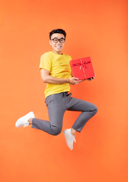 Asian man in yellow t-shirt jumping on orange background - Foto, Bild
