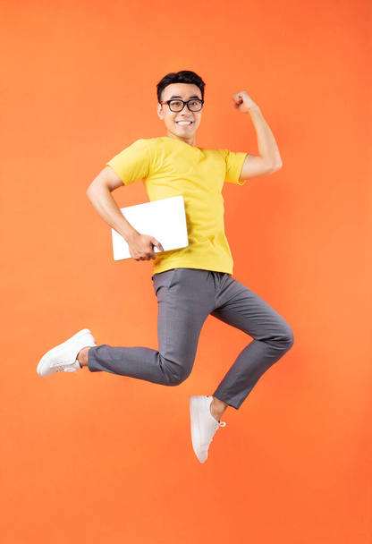 Hombre asiático en camiseta amarilla saltando sobre fondo naranja - Foto, Imagen