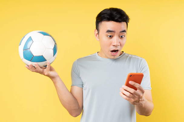 Азиатский мужчина держит мяч и телефон в руке - Фото, изображение