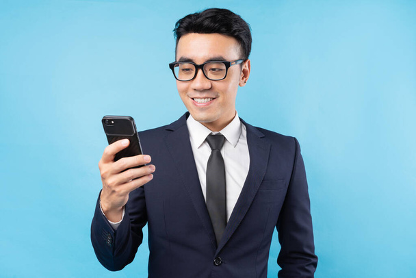 Buisnessman asiático con traje sosteniendo teléfono inteligente sobre fondo azul - Foto, imagen