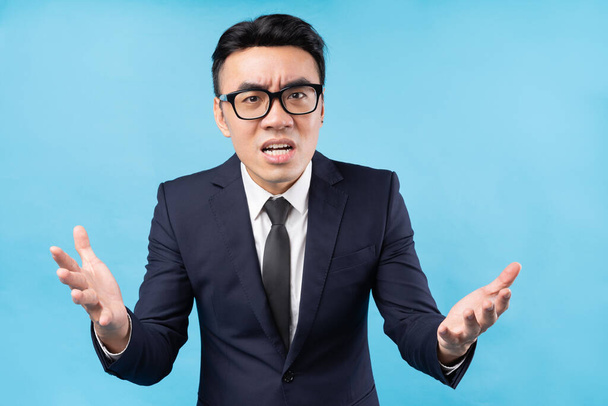 Азиатский бизнесмен в костюме злится на голубом фоне - Фото, изображение