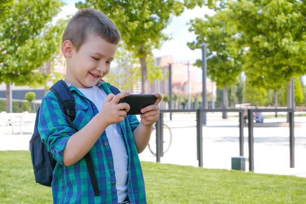 Happy schoolboy looking at smartphone screen and smiling, video call, online games on smart phone - Фото, изображение