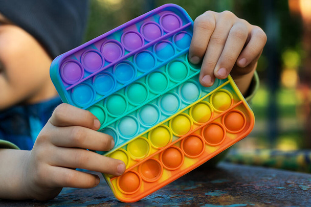 Ανώνυμο παιδί κρατά στα χέρια του αισθητηριακό παιχνίδι pop αυτό και το δείχνει μπροστά από τον εαυτό του.Χρώμα Rainbow.. - Φωτογραφία, εικόνα