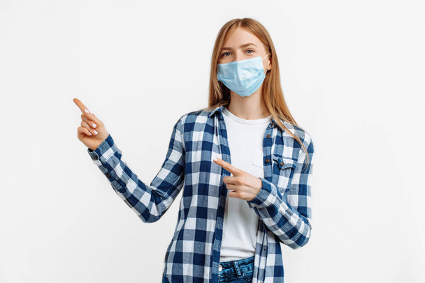 Young woman in medical protective mask pointing with finger to the side at copy space over isolated white background - Fotografie, Obrázek