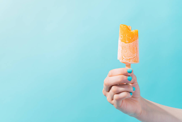 persona desconocida sosteniendo un helado naranja con un fondo azul. - Foto, Imagen