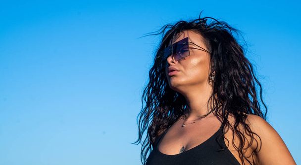 sexy brunette girl has long curly hair wearing stylish sunglasses and enjoy summer weather outdoor, fashion and beauty, copy space - Photo, Image