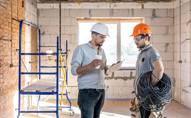 Two builder engineers talking at building site, engineer explaining a drawing to a worker. - 写真・画像