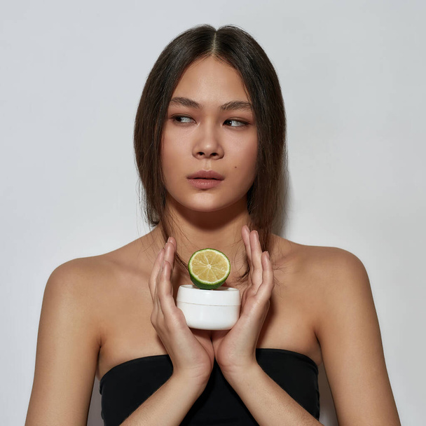 Joven mujer asiática sosteniendo cítricos y cosmetología crema - Foto, imagen