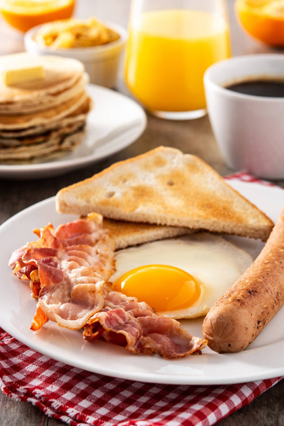 Tradycyjne amerykańskie śniadanie ze smażonym jajkiem, tostem, bekonem i kiełbasą na drewnianym stole - Zdjęcie, obraz