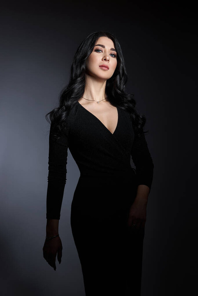 Beautiful brunette woman in a black dress poses in the studio. Elegant girl with beautiful natural makeup - Fotó, kép