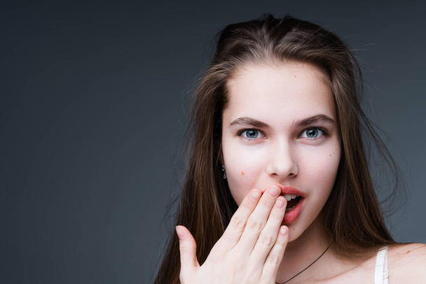 Attractive girl is surprised looking into the camera and applying a hand to her mouth. Isolated on dark background - Foto, imagen