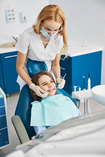 Blonde dental working over child teeth with instruments - Photo, image