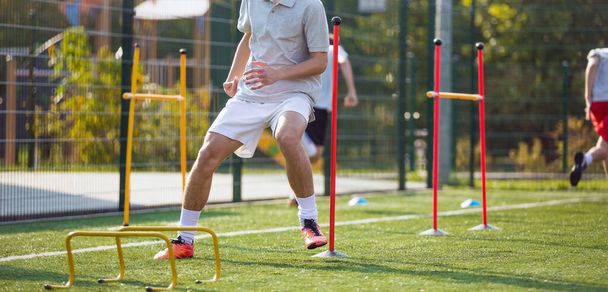 Teenage Football Players on Training Camp. Young Boys Running Slalom Track Between Training Poles and Jumping Over Hurdles. Soccer Training Equipment - Zdjęcie, obraz