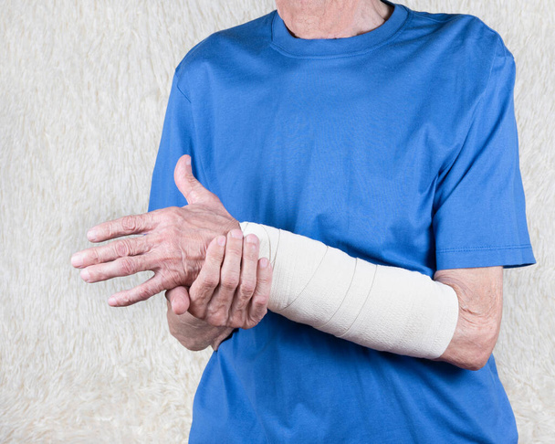 Male hand holding wrist with bandage. Eldery man suffering from pain in hand. Bone disease.  White background.   - Foto, afbeelding