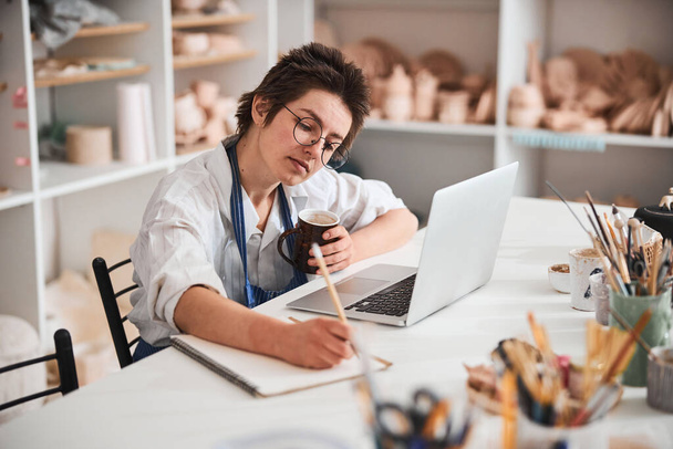 Smart pottery shop owner writing in notebook - 写真・画像