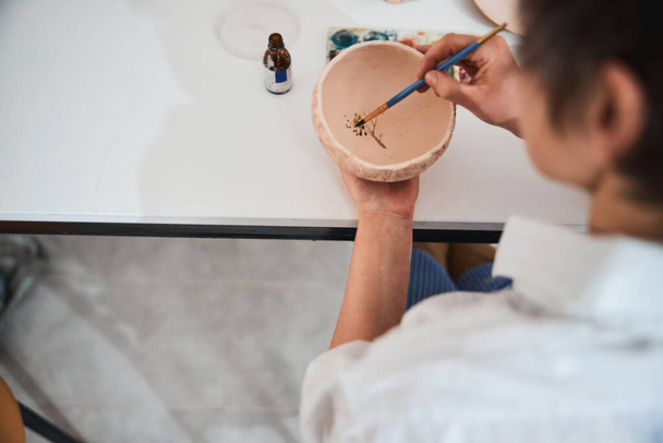 Trabajador en tienda de cerámica pintando hojas de árbol en tazón de barro - Foto, imagen