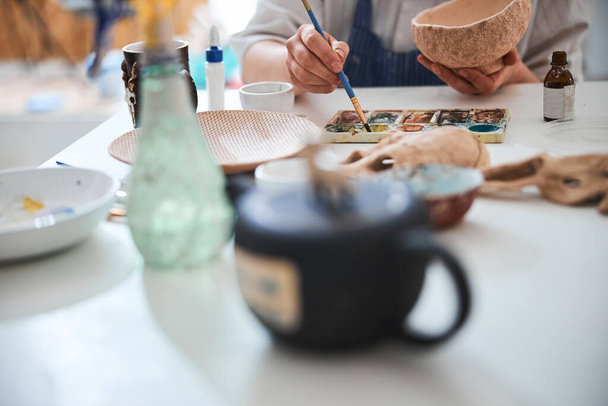 Adult reaching for paint with brush during pottery painting - 写真・画像