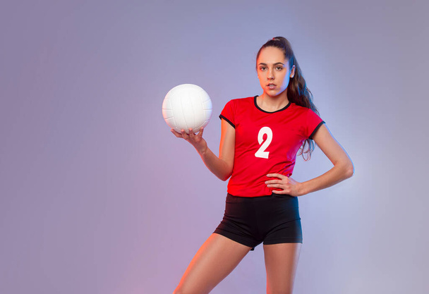 Βόλεϊ κορίτσι κρατήσει και να κλωτσήσει μπάλα σε νέον φόντο. Παίκτης που κάνει γυμναστική στο σπίτι. Έννοια αθλητισμού και αναψυχής - Φωτογραφία, εικόνα