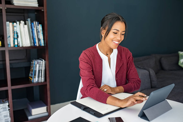 Portrait of mature executive businesswoman using digital tablet while working from home. African mature woman working on laptop at home. Happy smiling mid adult woman making notes in smart working. - Foto, Bild
