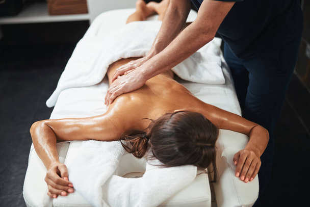 Charming elegant brunette woman receiving professional healing body treatment in wellness center - Фото, изображение