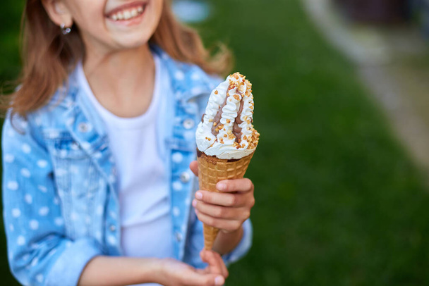 Cute girl with italian ice cream cone smiling and looking at camera while resting in park on summer day, child enjoying ice cream outdoor, happy holidays, summertime - Foto, immagini