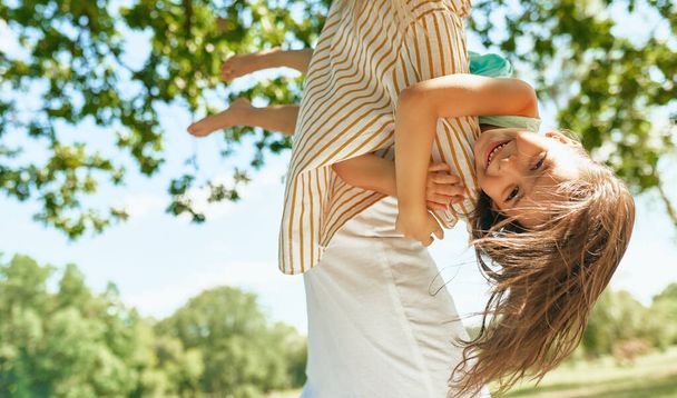 A mother and her joyful little girl playing in the park during the picnic. Happy woman and daughter smiling and spending time together on a sunny day. Mother's day concept. - Photo, Image
