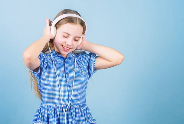 Immersing in music. Adorable child enjoy music playing in earphones on blue background. Little girl enjoying her favorite music. Cute kid listening to music playing in headphones, copy space - Photo, image