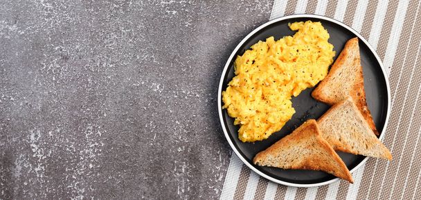 Scrambled eggs with toast on a round plate on a dark background. Top view, flat lay - Photo, Image