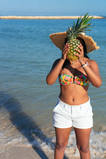 Donna con un ananas sul viso cammina sulla spiaggia - Foto, immagini
