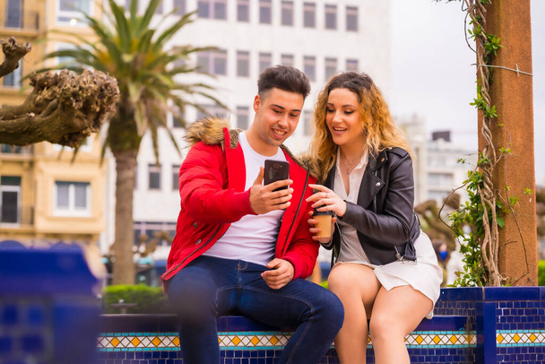Lifestyle of a Caucasian couple doing vacation tourism, in a city park looking at things on the internet with the mobile - 写真・画像
