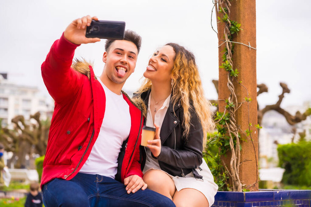 Lifestyle of a Caucasian couple sightseeing on vacation, in a city park smiling and taking a picture with the phone - 写真・画像
