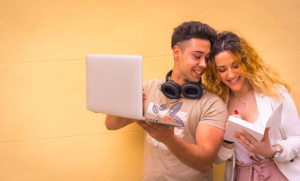 Young entrepreneur couple doing teamwork with a computer. With a yellow background, boy in music headphones and girl in white suit - Фото, зображення