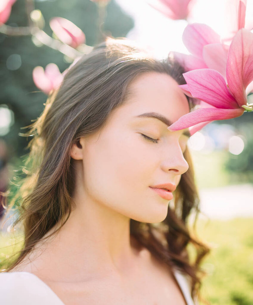 Portrait of young woman in spring garden among blooming magnolia tree with closed eyes. - Photo, Image