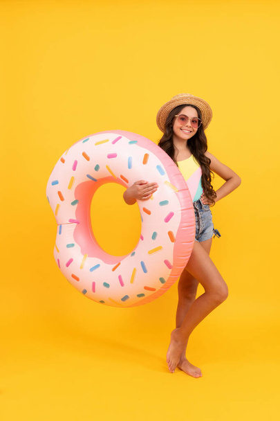 glückliches Mädchen mit Strohhut und Sonnenbrille aufblasbaren Donut-Ring. Kind hält Strand-Accessoire - Foto, Bild