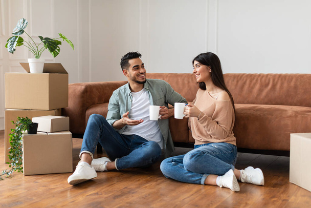 Ευτυχισμένος άντρας και γυναίκα πίνουν καφέ καθισμένοι στο πάτωμα. - Φωτογραφία, εικόνα