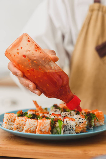 Chef knijp saus op een set sushi broodjes met roomkaas, rijst en zalm. Sushi rollen productieproces - Foto, afbeelding