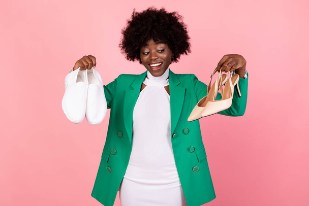 Afro-Amerikaanse winkelverslaafde vrouw kiezen trendy schoenen over roze achtergrond - Foto, afbeelding