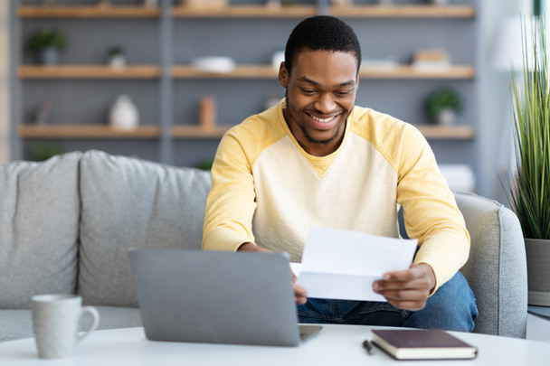 Sonriente hombre afroamericano leyendo carta en casa - Foto, imagen