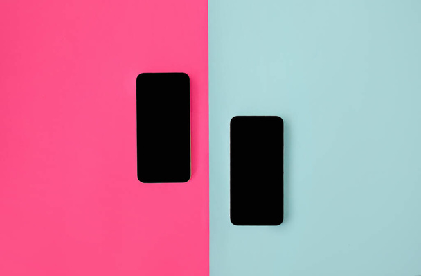 Два смартфона з порожніми екранами на синьо-рожевому фоні, вид зверху, плоский
 - Фото, зображення