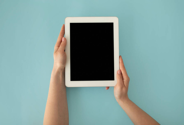 Vrouwelijke handen houden digitale tablet computer met mockup voor uw ontwerp op blanco scherm op blauwe achtergrond, bovenaanzicht. - Foto, afbeelding
