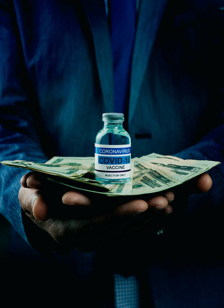 シミュレーションされたcovid-19ワクチンボトルとたくさんのドル紙幣を手にした若い白人ビジネスマンの閉鎖 - 写真・画像