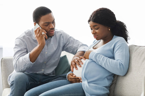 Worried black husband calling doctor while wife having labor pains - Zdjęcie, obraz