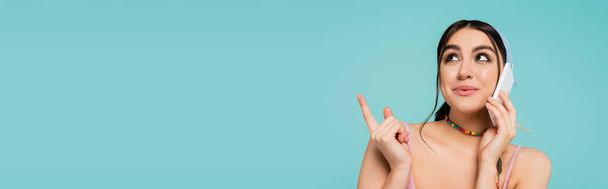Young woman talking on smartphone and pointing with finger isolated on blue, banner  - Foto, immagini