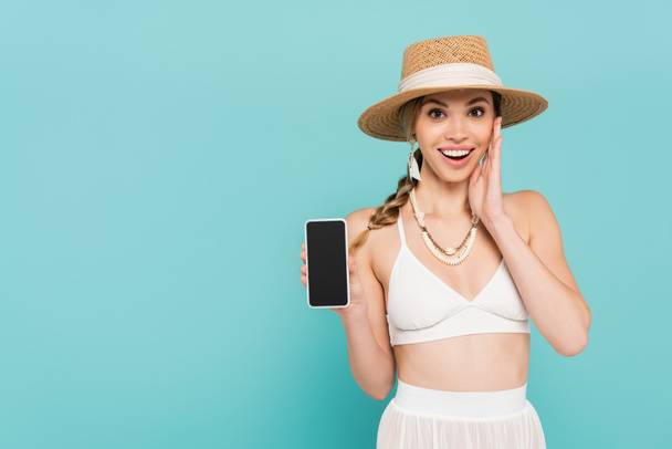 Cheerful woman in sun hat holding smartphone with blank screen isolated on blue  - Фото, изображение