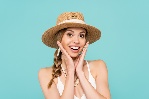Χαρούμενη γυναίκα με ψάθινο καπέλο κοιτάζοντας την κάμερα απομονωμένη στο μπλε  - Φωτογραφία, εικόνα