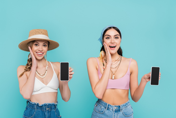 Positive women in tops holding smartphones isolated on blue  - Photo, Image
