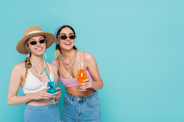 Smiling women in sunglasses holding cocktails isolated on blue  - Photo, Image