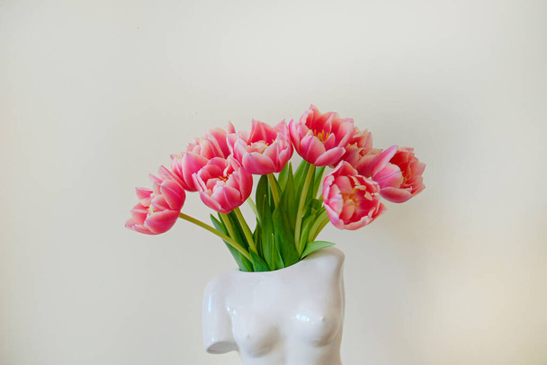 Conceptual image of bi-color tulips bouquet in ceramic venus de milo shaped vase over white wall background with a lot of copy space for text. Close up. - Foto, imagen